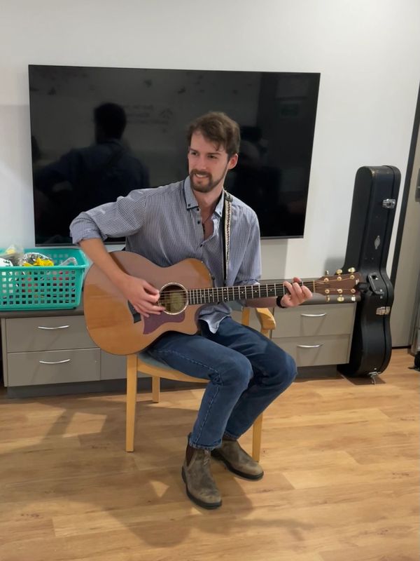 Young man smiling while seated, playing acoustic guitar.