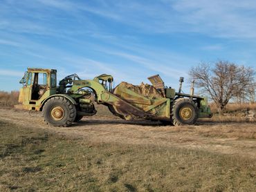 Old green Terex TS-14 loader filled with dirt on a dry field.