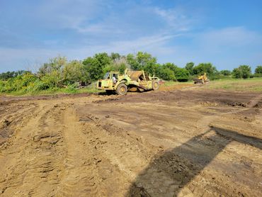 Construction vehicles working on a dirt field under a clear sky.