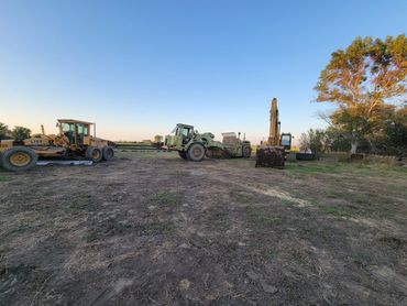 Three heavy construction vehicles parked on a dirt field at sunset.