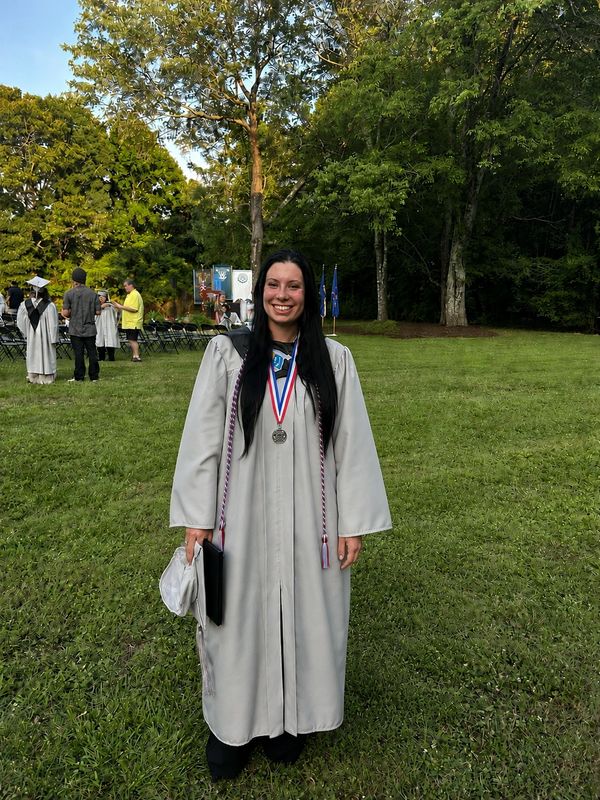 Graduate in cap and gown smiling outdoors.