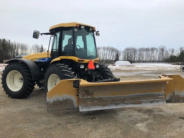 A yellow and black tractor with a mounted snow blade