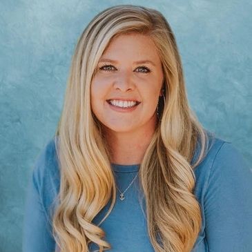 Smiling blonde woman in blue shirt with wavy hair.