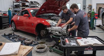 Two mechanics working on a red sports car engine in a workshop.