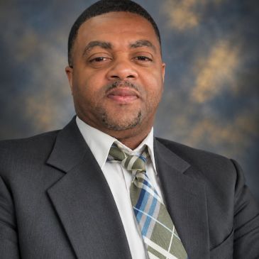 Man in a suit and plaid tie against a blurred background.