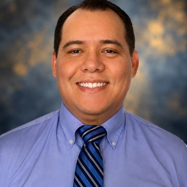Man in a blue shirt and striped tie smiling.