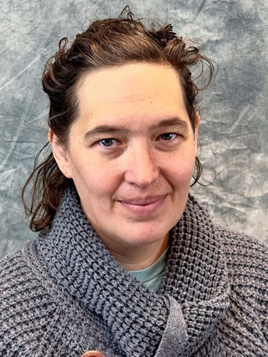 Person with curly hair wearing a gray knitted scarf.