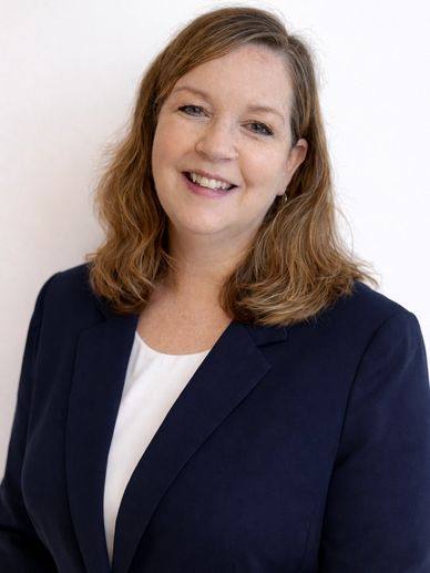 Smiling woman with light brown hair in a navy blazer.