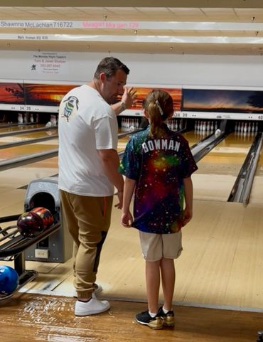 An adult teaching a child how to bowl at a bowling alley.