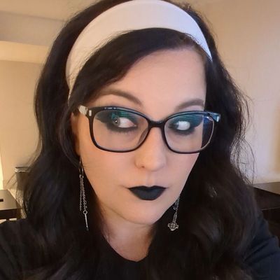 Woman with black lipstick, glasses, and a white headband looking sideways.