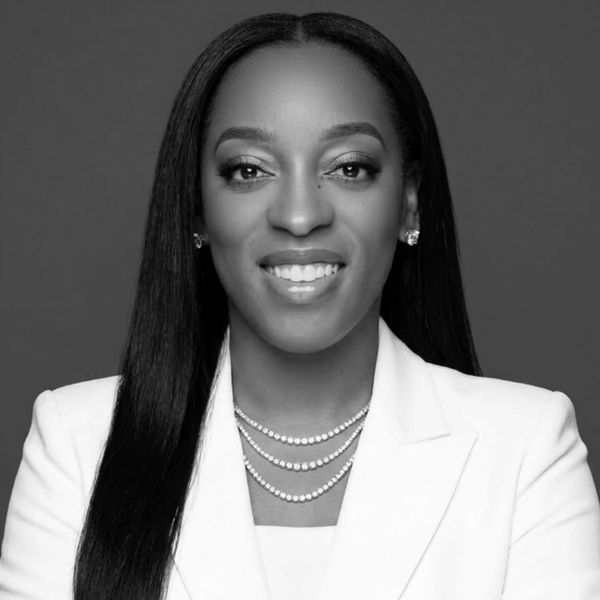 Professional black and white portrait of a confident woman in a white blazer and layered pearl necklace.