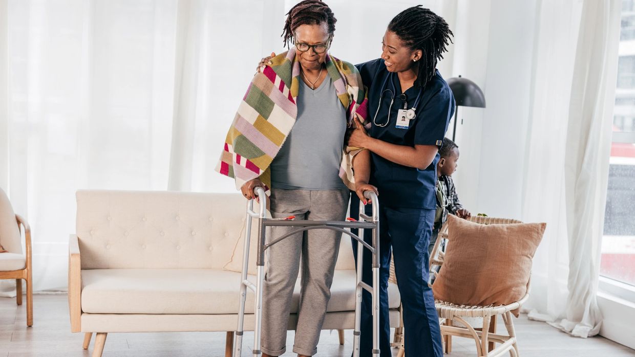 Nurse assisting elderly woman with walker.