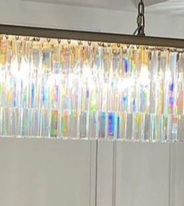 Modern dining room with a sleek chandelier and beige chairs around a dark table.