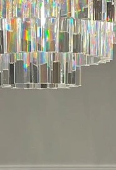 Elegant crystal chandelier above a black fireplace with wall sconces and a potted orchid.