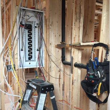 Electrical panel installation in unfinished wooden framing with tools and wires.