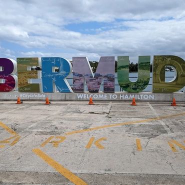 Colorful Bermuda sign reading 'Welcome to Hamilton' at the waterfront with a cloudy sky backdrop.