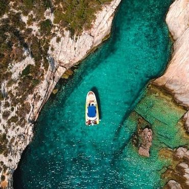 Aerial view of boat sailing through narrow turquoise waterway between rocky cliffs.