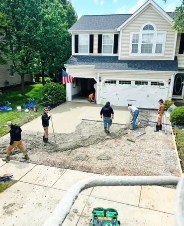 Workers pouring and leveling concrete for a new driveway at a suburban house.