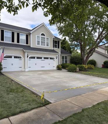 Newly paved driveway in front of a suburban house with two white garage doors.