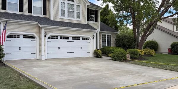 Newly paved concrete driveway in front of a two-car garage attached to a suburban house.