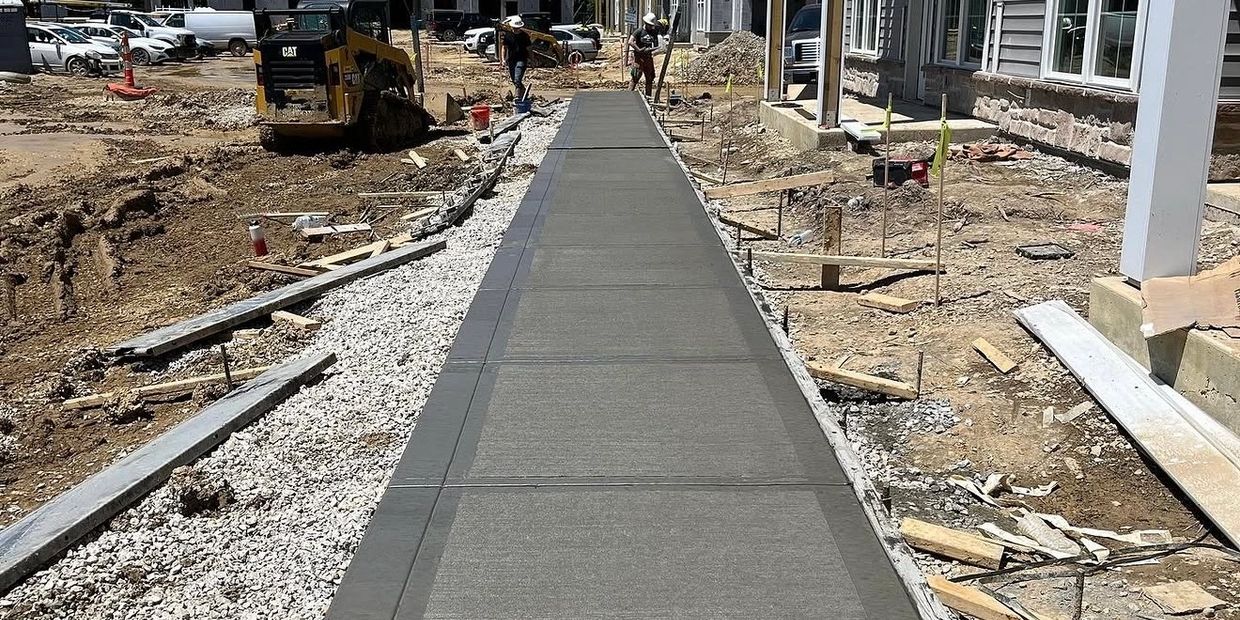 Newly poured concrete sidewalk at a construction site beside buildings.