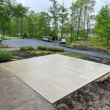 Freshly poured concrete slab in a green, outdoor setting near golf carts.