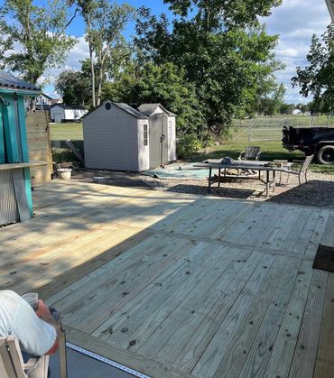 Newly built wooden deck in a backyard with a shed and outdoor seating.
