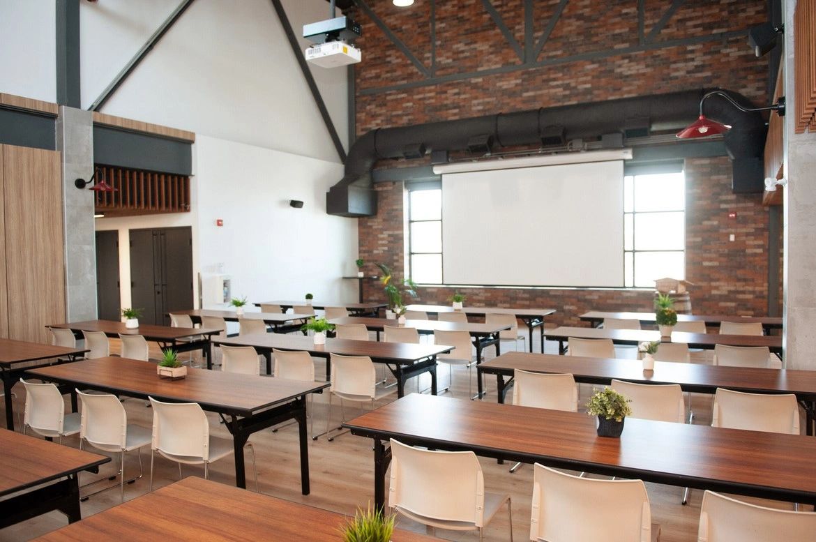 Modern classroom with wooden tables, white chairs, and a projector screen.
