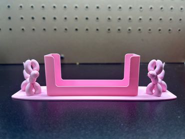 Pink 3D-printed object with two balloon animal-like figures on each side.