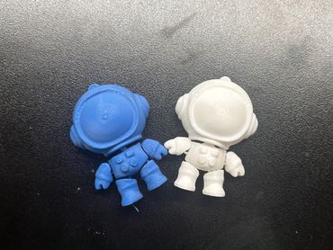 Two small astronaut figurines, one blue and one white, on a black surface.