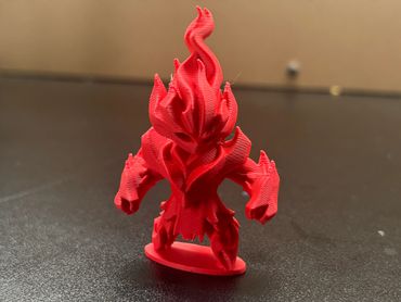 Red 3D-printed fiery creature figurine on black surface.