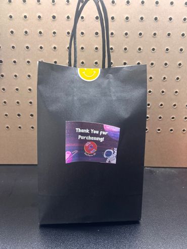 Black paper bag with thank you sticker and smiley seal on top.