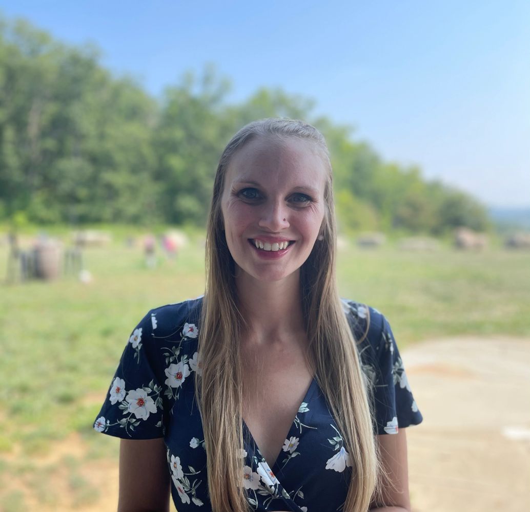 Blonde, therapist smiling at the camera wearing a flowery flow-y dress with mountains