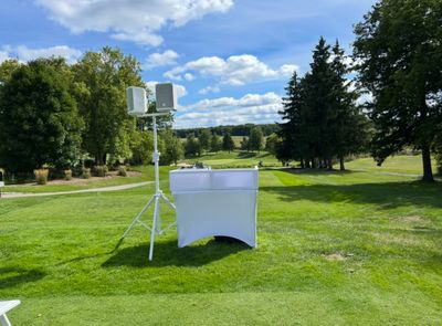 Outdoor DJ setup on a lush green golf course under a blue sky.