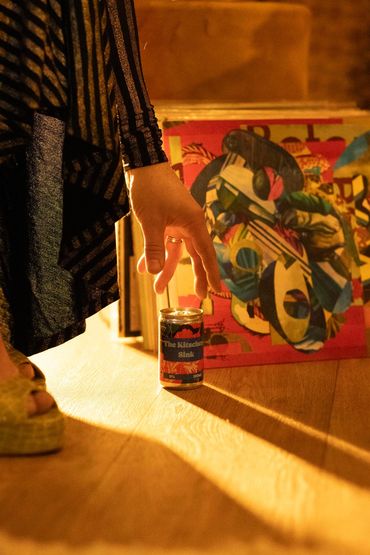 hand reaching for a bespoke canned cocktail called The Kitchen Sink next to high heel