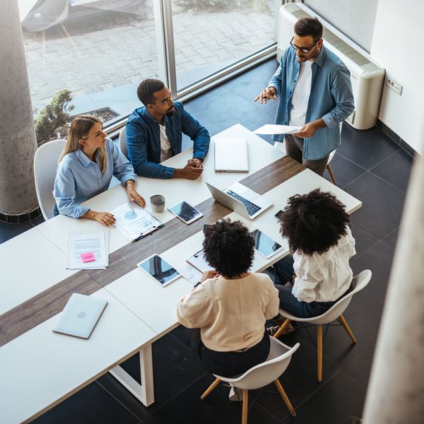 A group of five professionals engaged in a meeting around a modern table with laptops, documents