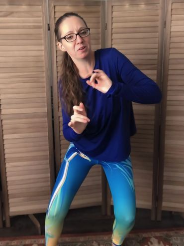 A woman in a blue top and vibrant leggings poses dynamically in front of wooden panels.