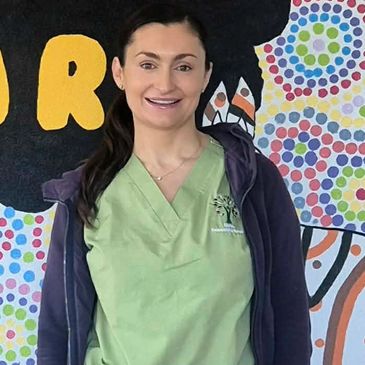 Smiling woman in green scrubs and a purple hoodie.