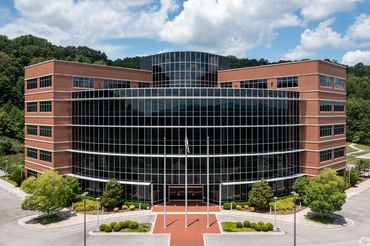 Modern office building with glass facade and brick exterior under a partly cloudy sky.