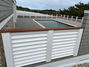 Modern pool deck with white louvered railing and scenic background.