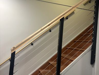 Modern wooden staircase with metal cable railing and light-colored handrail.