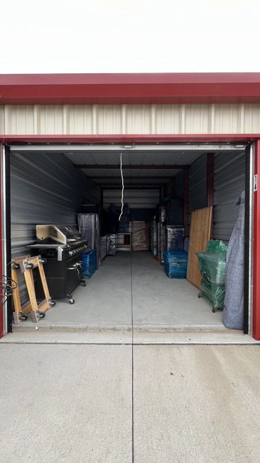 Open storage unit with wrapped furniture and a grill inside.