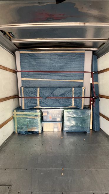 Furniture and boxes secured inside a moving truck with straps and protective covers.