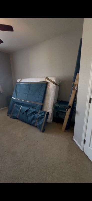 Furniture wrapped in blue moving blankets in an empty room.