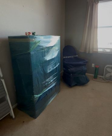 Furniture wrapped in protective covers in a sparsely furnished room.