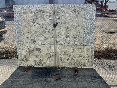 Large granite slabs secured with straps against a fence outdoors.