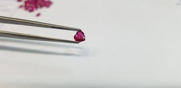 Heart-shaped pink gemstone held by tweezers against a white background.