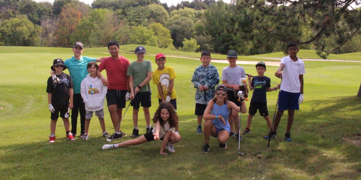twelve boys and girls posing on the golf course at camp holding golf clubs and smiling