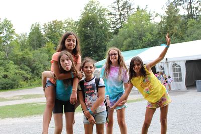 five girls making silly faces and smiling while posing near a large white tent