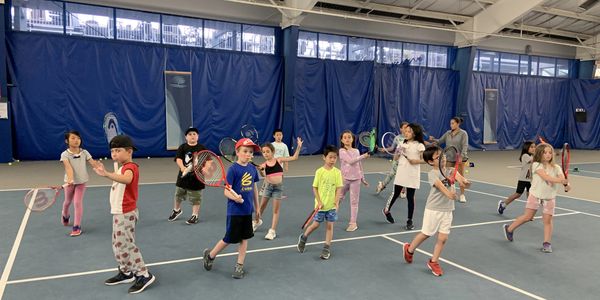 large group of kids practicing tennis drills on an indoor court